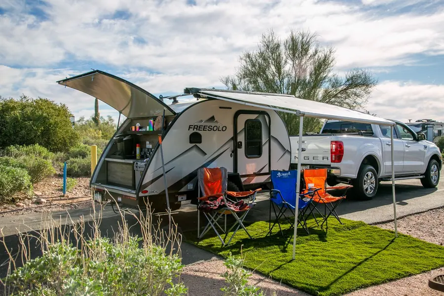 Compact travel trailer with the awning out and camp chairs set up beside a pickup truck