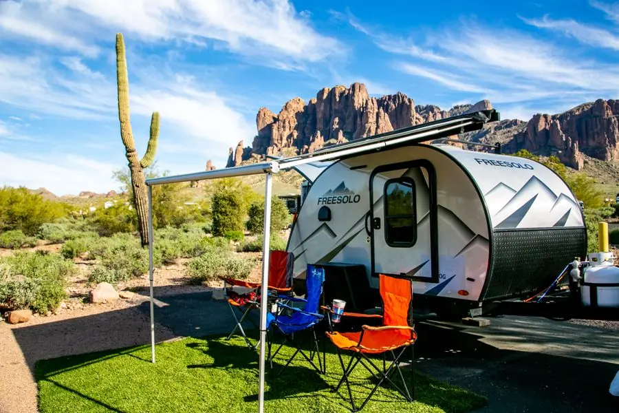 Travel trailer with its awning extended at a desert campsite, saguaro cactus and red rock bluffs behind